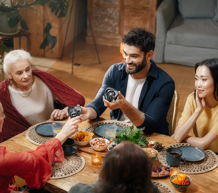Persone di diverse nazionalità riunite attorno a un tavolo, gustando un pasto e impegnandosi in vivaci discussioni, creando un'atmosfera calda e accogliente mentre si passavano gli auricolari Vasco Translator E1.