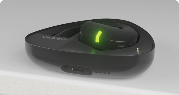 Un auricolare Vasco Translator E1 è inserito nella sua custodia di ricarica. Gli indicatori LED lampeggianti mostrano il livello di carica attuale della custodia e dell'auricolare. 