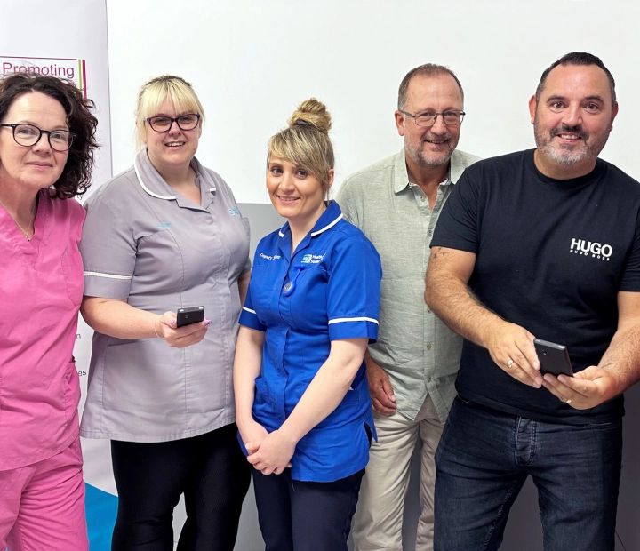 Cinque persone sorridenti sono in piedi insieme con abbigliamento sanitario, e due di loro tengono in mano un dispositivo di traduzione.