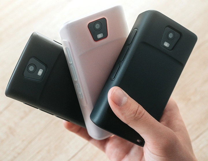 Persona che tiene tre dispositivi Vasco Translator Q1 con custodie in silicone, mostrando tre diversi colori: Solid Black, Dark Caramel, e Milky White.